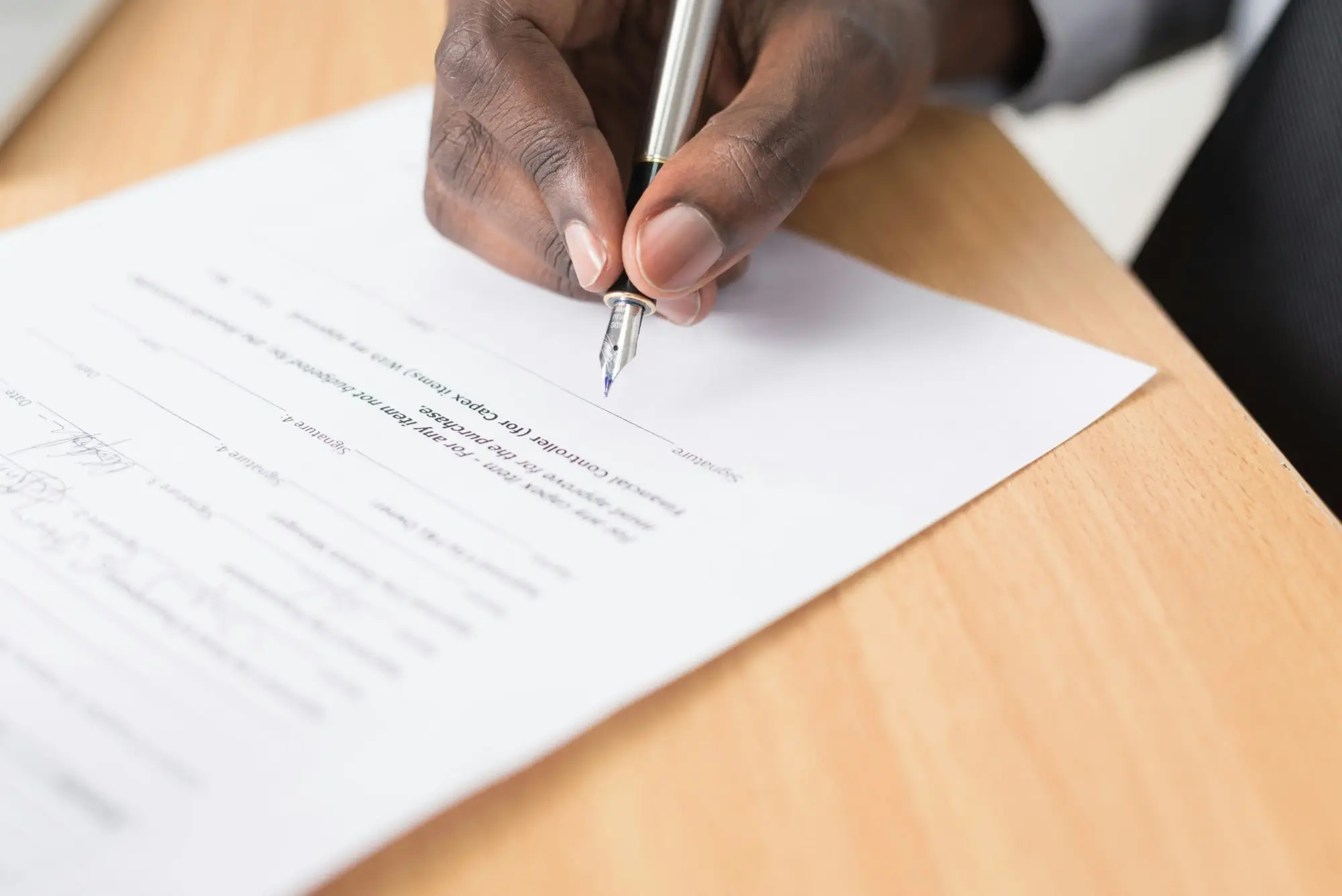 Close-up of a hand signing a document with a fountain pen on a wooden desk