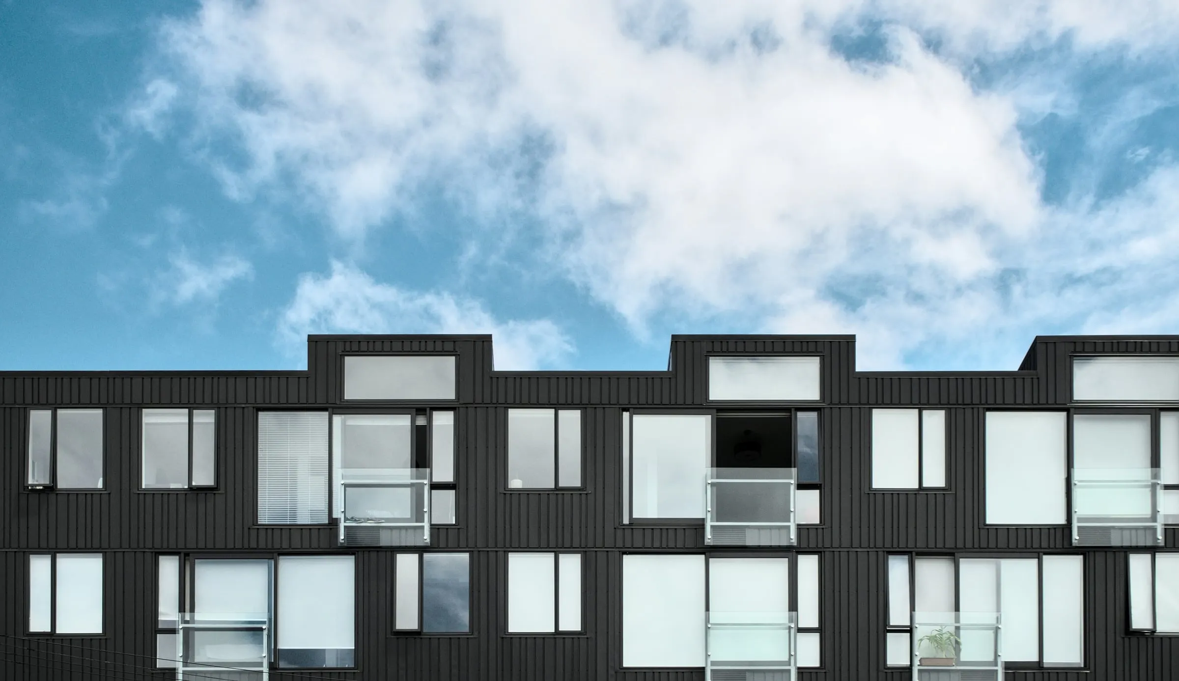 Contemporary dark multifamily residential building against a cloudy sky