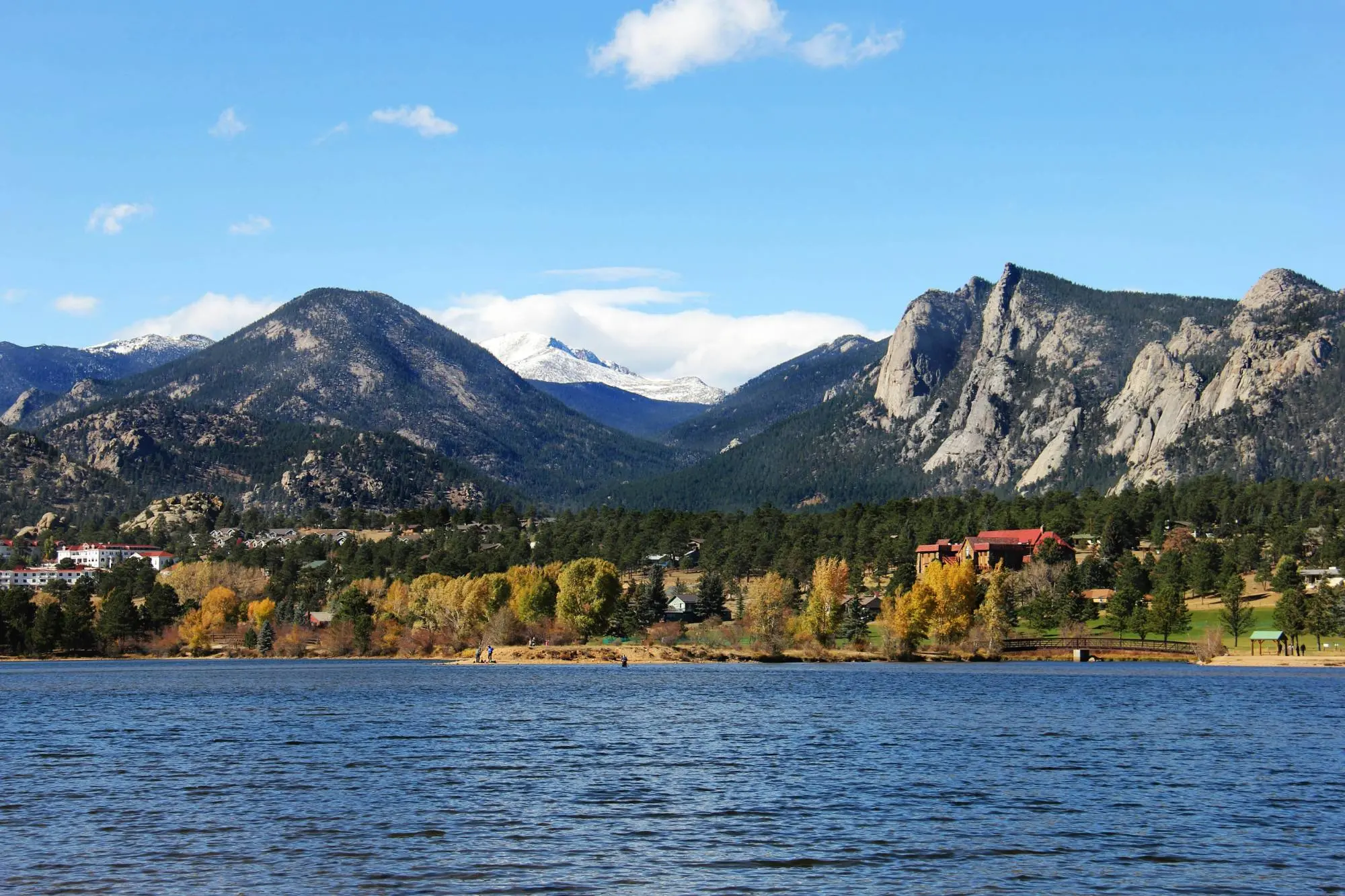 A mountain lake lined with autumn trees and homes beneath rocky peaks